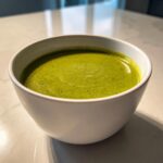 A close-up of a white bowl filled with vibrant, creamy roasted broccoli soup.