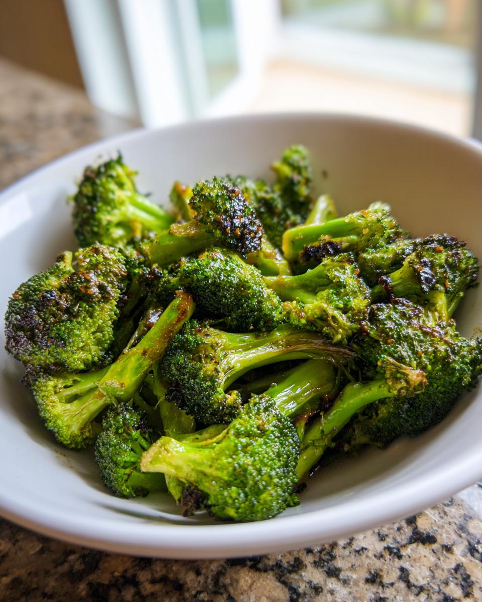 Close-up of perfectly roasted broccoli florets coated in a shiny roasted broccoli vinegar mustard glaze, served in a white bowl.