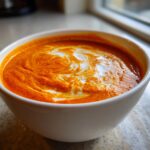 Close-up of vibrant orange roasted red pepper soup with a swirl of cream or melted Gouda.