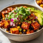 Close-up of a vibrant roasted sweet potato taco bowl featuring seasoned sweet potato cubes, black beans, corn, red onion, and cilantro.