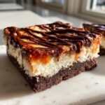 A rich, layered square of samoa cheesecake bars featuring a brownie base, creamy filling, caramel, and chocolate drizzle.