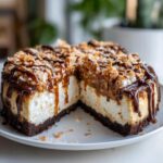 A rich slice taken out of a Samoa Cheesecake topped with toasted coconut, caramel, and chocolate drizzle.