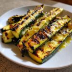 Close-up of perfectly grilled zucchini spears topped with melted, browned cheese.
