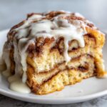 Close-up of a thick slice of sheet pan cinnamon roll pancakes, layered with cinnamon filling and drizzled heavily with white icing.