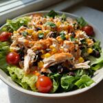 A vibrant bowl of high protein salad featuring shredded chicken, black beans, corn, and cherry tomatoes with an orange dressing.