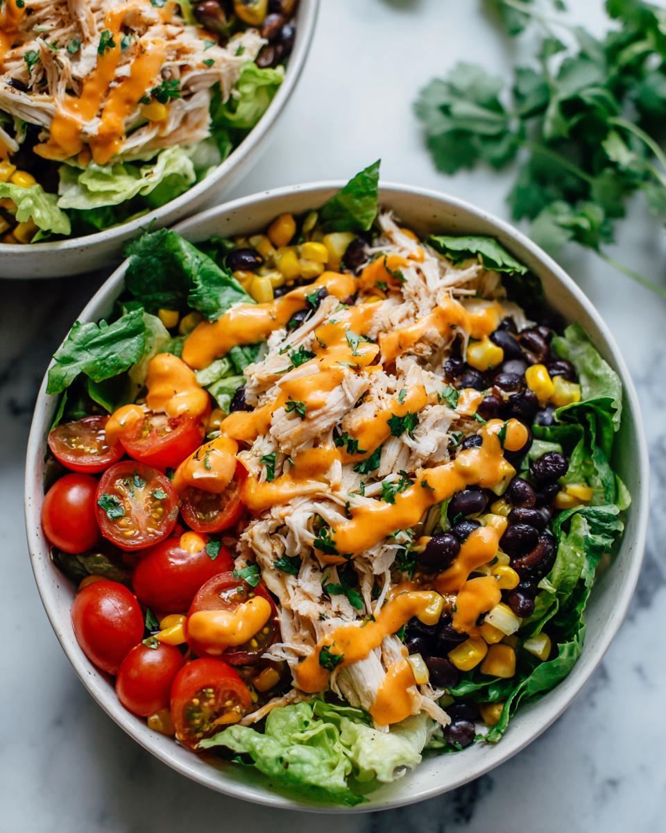 Close-up of a vibrant high protein salad featuring shredded chicken, black beans, corn, tomatoes, and an orange dressing.