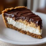 Close-up of a decadent slice of peanut butter pie showing graham cracker crust, whipped cream, peanut butter layer, and chocolate ganache.