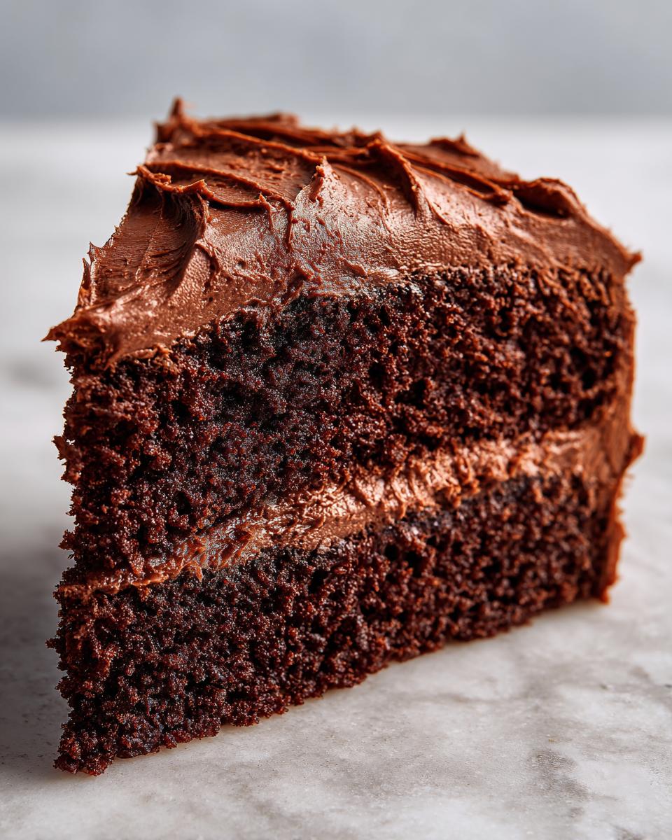 Close-up of a rich, dark chocolate cake slice generously covered in thick chocolate ganache frosting.