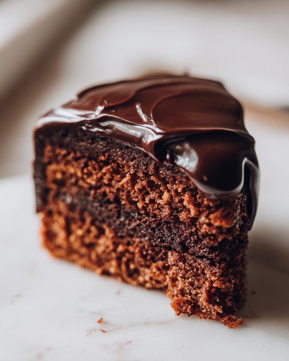 Close-up of a rich chocolate cake slice covered in glossy, smooth chocolate ganache.