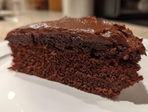 Close-up of a moist, dark chocolate cake slice topped with thick, shiny chocolate ganache.