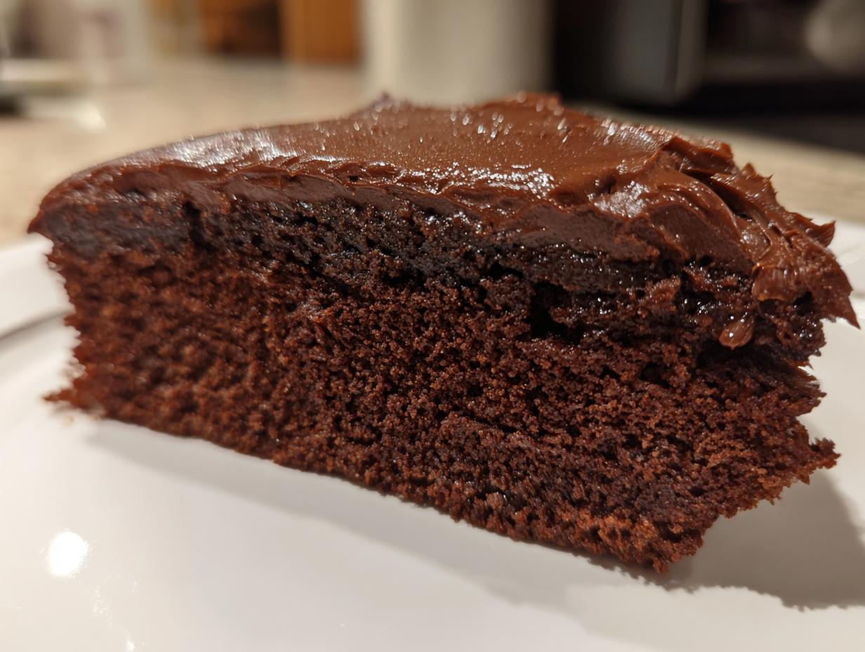 Close-up of a moist, dark chocolate cake slice topped with thick, shiny chocolate ganache.