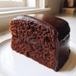 A rich slice of dark chocolate cake generously covered in smooth, shiny chocolate ganache.