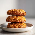 Three soft pumpkin oatmeal cookies stacked vertically on a small, light-colored plate.
