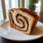 A thick, beautifully swirled slice of sourdough cinnamon swirl bread resting on a white plate.