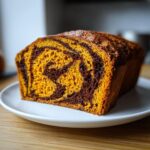 A close-up of a loaf of sourdough pumpkin cinnamon swirl bread showing the vibrant orange pumpkin batter swirled with dark chocolate batter.