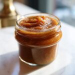 Close-up of a small glass jar filled with rich, dark brown spiced pear butter.
