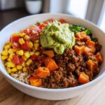 A close-up of a delicious sweet potato taco bowl topped with ground meat, corn salsa, and a dollop of guacamole.