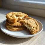 A stack of thick and chewy white chocolate macadamia nut cookies, one broken open to show the gooey center.