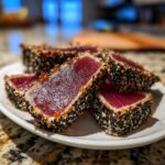 Slices of seared tuna tataki coated in black and white sesame seeds on a white plate.