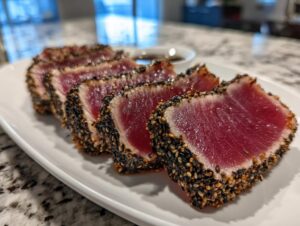 Close-up of perfectly seared tuna tataki slices coated in black and white sesame seeds, served on a white platter.