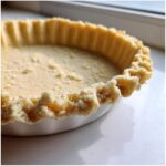 Close-up of an unbaked, flaky pie crust recipe pressed into a white tart dish, showing crimped edges.