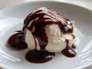 A scoop of vanilla ice cream generously covered in rich, glossy chocolate sauce on a white plate.