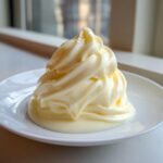 A close-up of a beautiful swirl of smooth, pale yellow white chocolate ganache on a white plate.