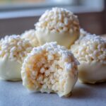 Close-up of white chocolate rice krispie balls, one with a bite taken out showing the crispy interior.