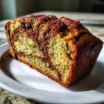 A close-up of a moist slice of zucchini cinnamon swirl bread showing the green zucchini shreds and dark cinnamon swirl.