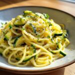 A close-up shot of a bowl of creamy zucchini pasta topped with grated cheese and fresh herbs.