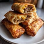 A stack of crispy, golden air fryer cheeseburger egg rolls, with the top two cut open revealing ground beef and melted cheese filling.