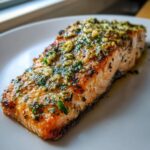 Close-up of a perfectly cooked baked salmon fillet topped with a glistening garlic and herb butter sauce.