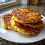 A stack of four golden-brown, crispy potato pancakes served on a white plate.