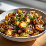 Close-up of a white bowl filled with golden roasted potato salad mixed with red onion and fresh parsley.