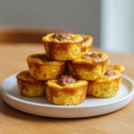 A stack of golden brown sausage egg bites with a piece of sausage topping, served on a speckled white plate.
