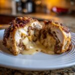Cross-section of a baked apple and brie stuffed chicken breast showing melted brie oozing out with chunks of apple filling.