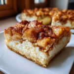 Close-up of a thick slice of apple cheesecake bars with crescent rolls, showing creamy filling and cinnamon apple topping.