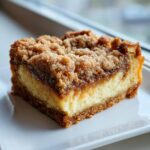 Close-up of a single serving of apple cheesecake bars showing the graham cracker crust, creamy cheesecake layer, and crumb topping.