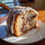 A close-up, sunlit slice of apple cinnamon roll cake recipe showing the swirl of cinnamon filling and thick white icing.