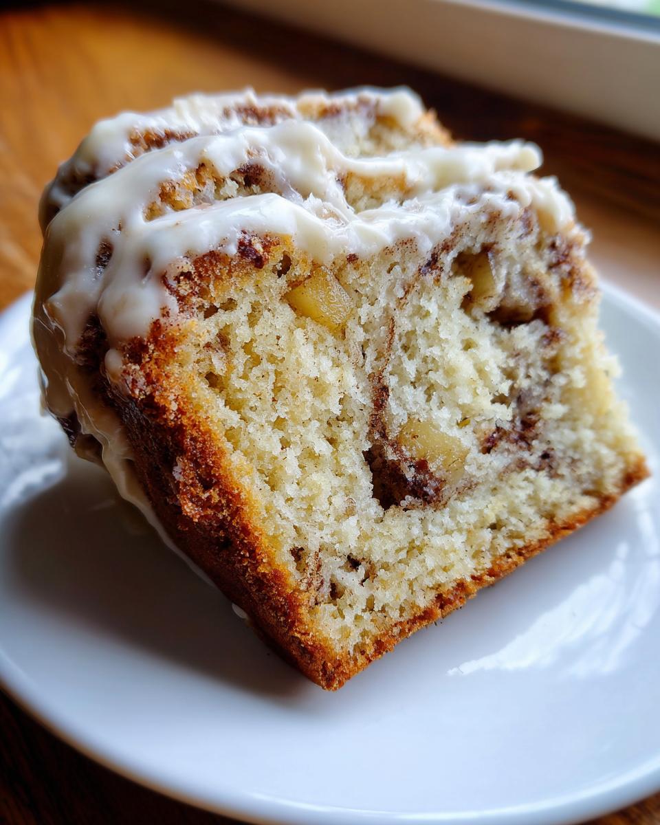 Close-up of a moist slice of apple cinnamon roll cake recipe topped with thick white icing.