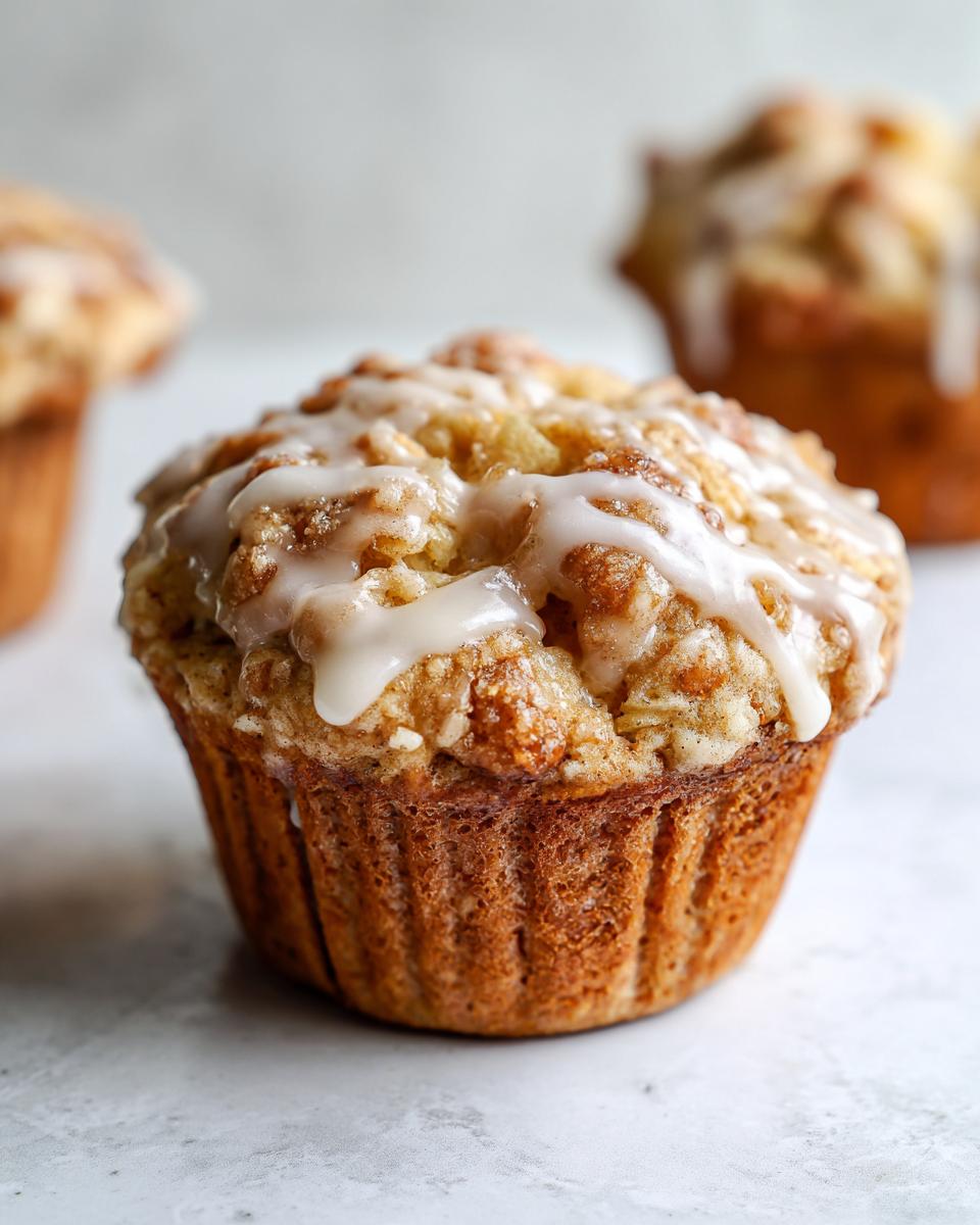 A close-up of one perfectly baked apple fritter muffins topped with crumb topping and a sweet vanilla glaze.