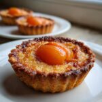 A close-up of a freshly baked apricot-almond tartlet with a golden-brown crust and glazed apricot halves on top.