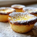 Four golden-brown baby lemon impossible pies dusted generously with powdered sugar.
