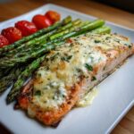 A perfectly cooked fillet of baked boursin salmon topped with melted cheese and herbs, served alongside roasted asparagus and cherry tomatoes.