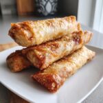 A stack of four crispy, golden brown cheeseburger egg rolls baked to perfection on a white plate.