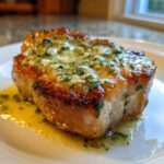 Close-up of a thick, juicy baked pork chops oven boneless topped with melted garlic butter and fresh parsley.