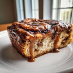A close-up of a moist slice of banana bread cinnamon rolls topped with thick, dripping caramel sauce.