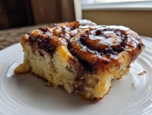 A close-up of a soft, glazed slice of banana bread cinnamon rolls served on a white plate.