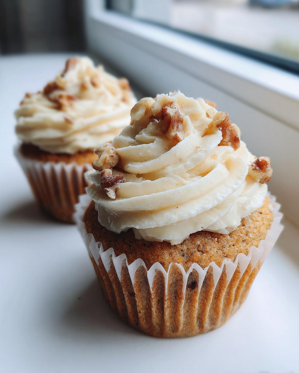 Close-up of two freshly baked banana walnut cupcakes topped with cream cheese frosting and chopped walnuts.