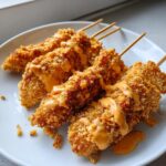 Four crispy, golden brown bang bang chicken skewers air fryer pieces drizzled generously with a creamy orange sauce on a white plate.